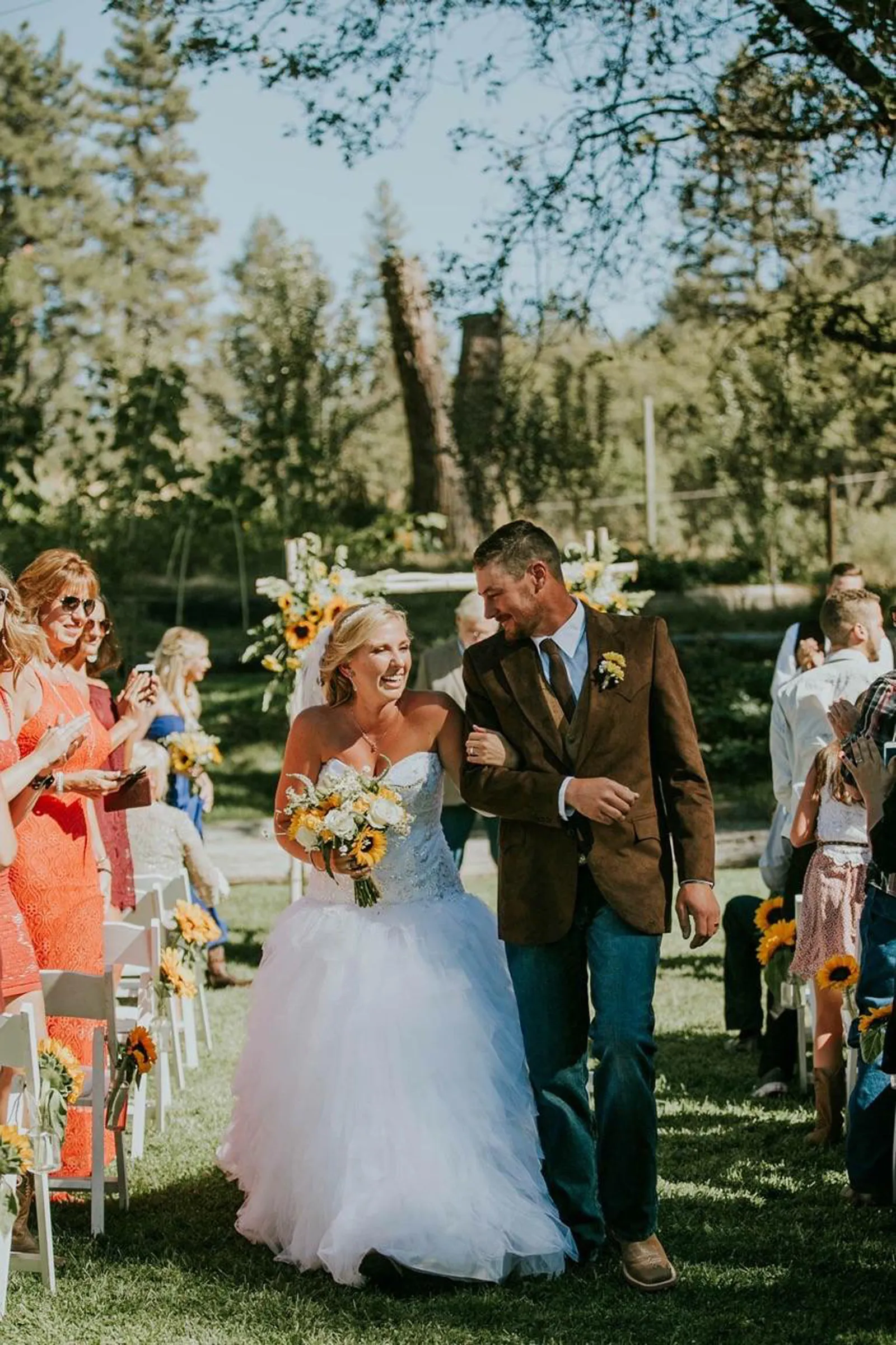 A bride and groom walking back down the aisle between guests and sunflower-tied chairs