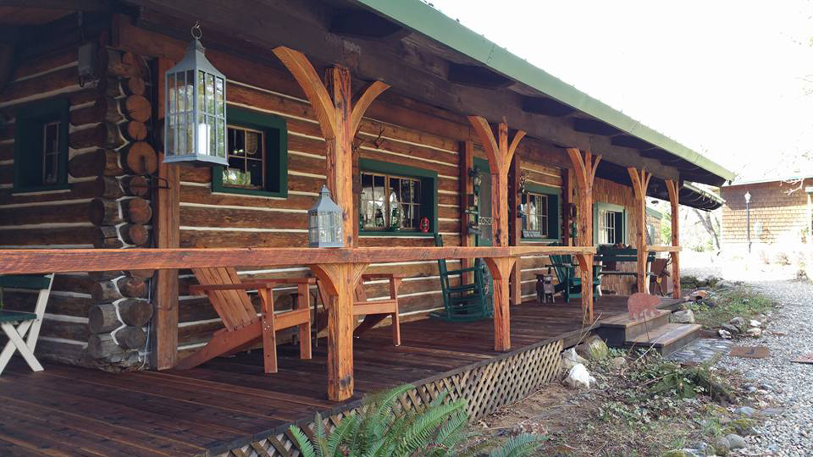 The covered log porch of the inn, with hand-cut log posts, lanterns and Adirondack chairs