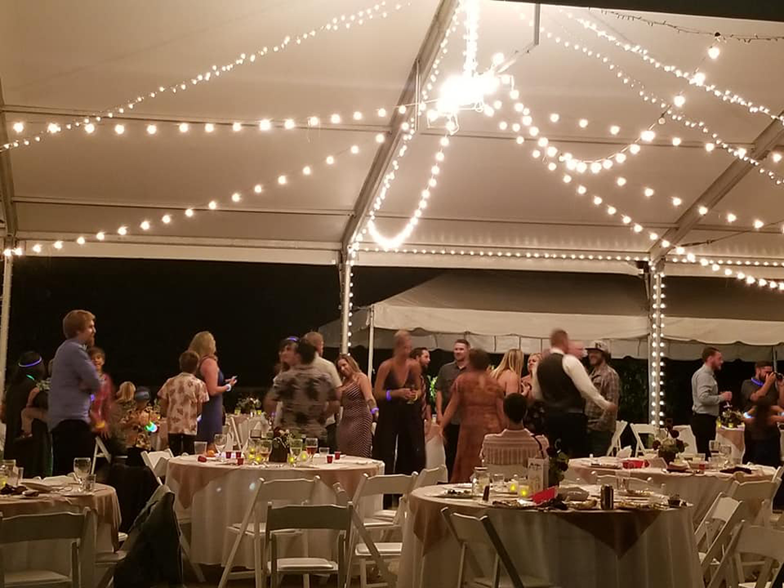 Guests under the reception tent at night, lit by strings of bulbs over round tables