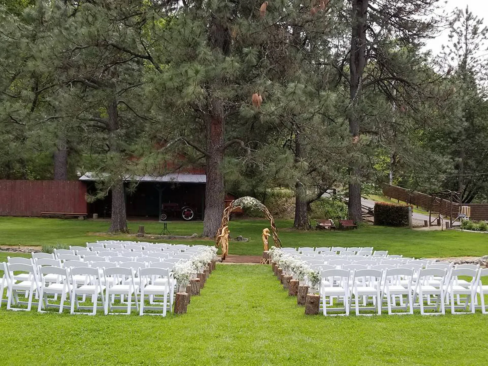 The ceremony lawn set with white chairs facing a manzanita-branch arch beneath tall pines