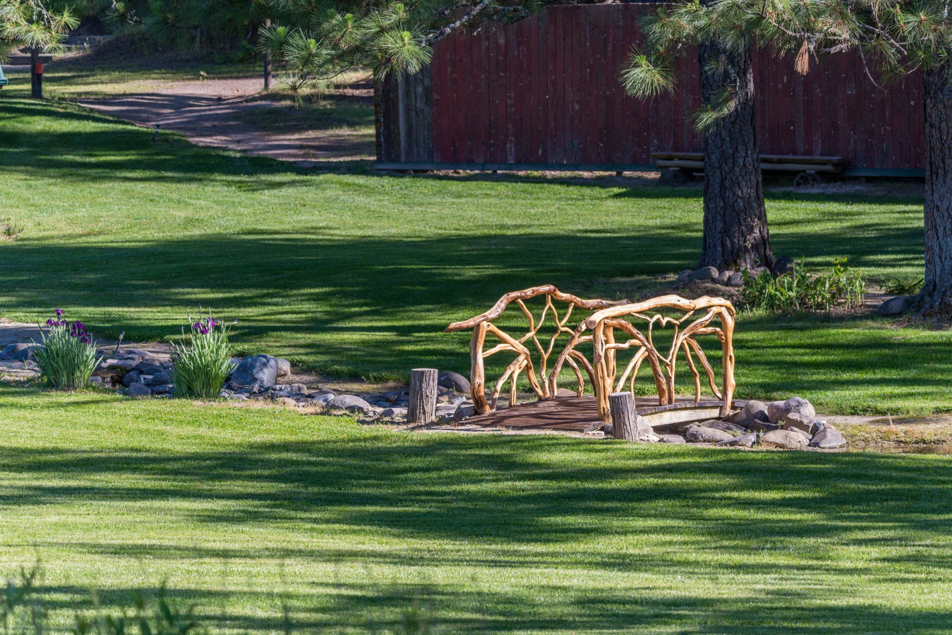 A handcrafted manzanita-branch footbridge crossing the creek on the ranch's mown lawn